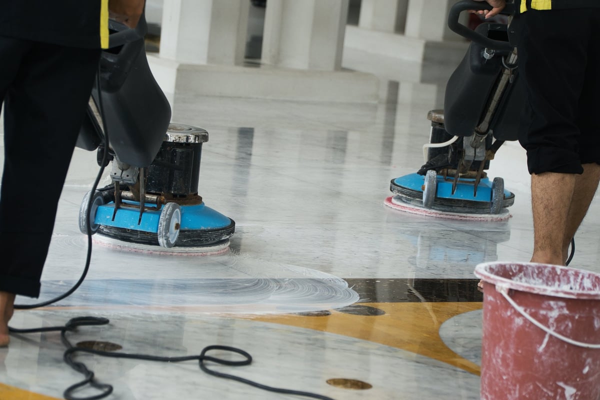 Two workers operate buffing machines to thoroughly clean a polished marble floor